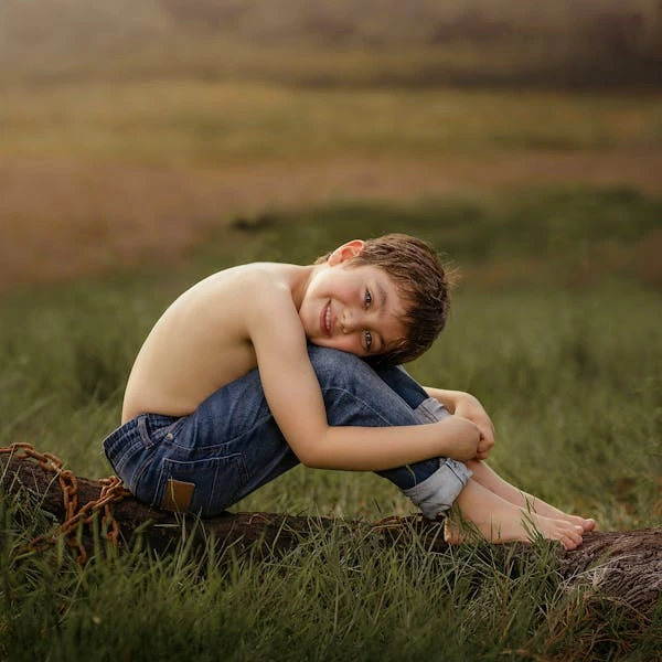 Happy Child Sitting on Log in Sunny Field